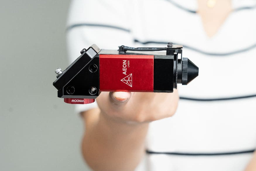 Red and black AEON camera lens held by a person with a blurred background